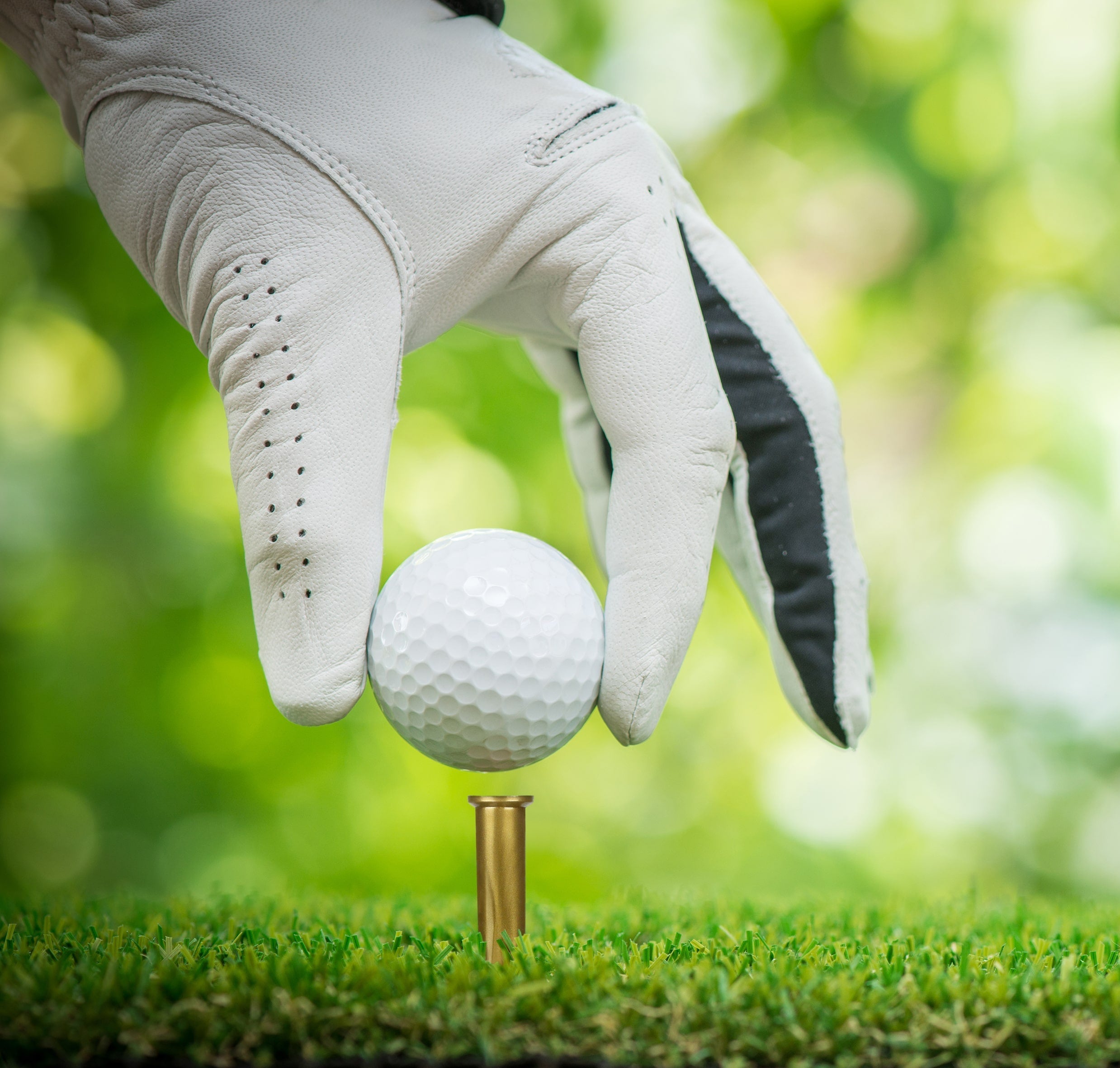 Golf ball on a tee with a gloved hand in the foreground, blurred green background