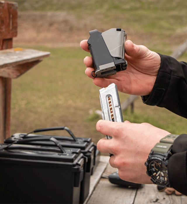 Shooter holding Maglula 22UpLULA .22LR magazine loader above a pistol magazine at an outdoor range