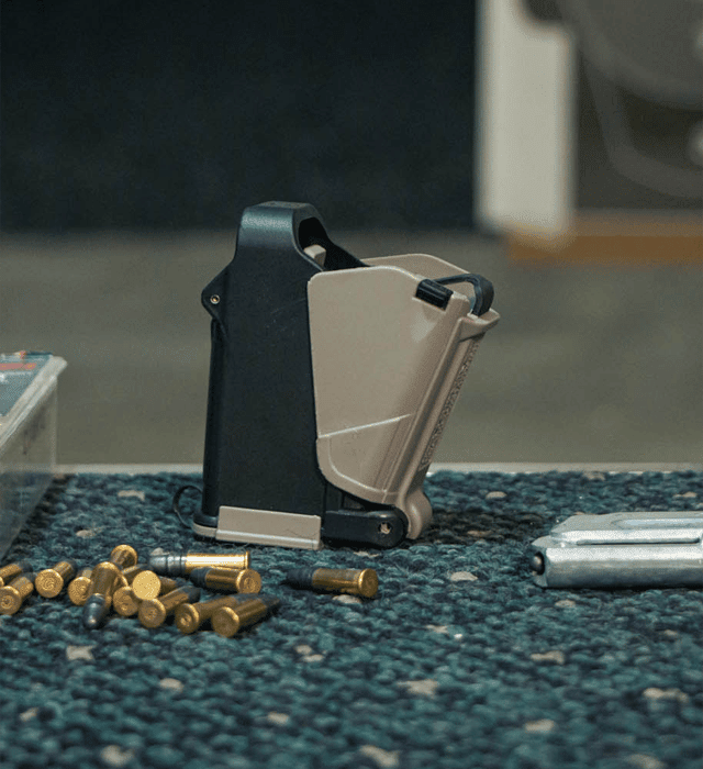 Maglula 22UpLULA .22LR magazine loader beside cartridges and pistol magazines on a range bench
