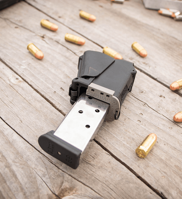 Black gun magazine on a wooden surface with bullets around