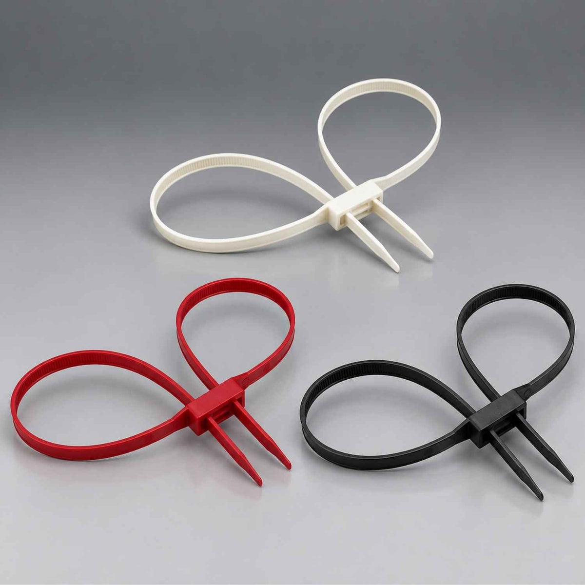 Three plastic zip tie handcuffs in white, red, and black, arranged on a smooth gray gradient background.
