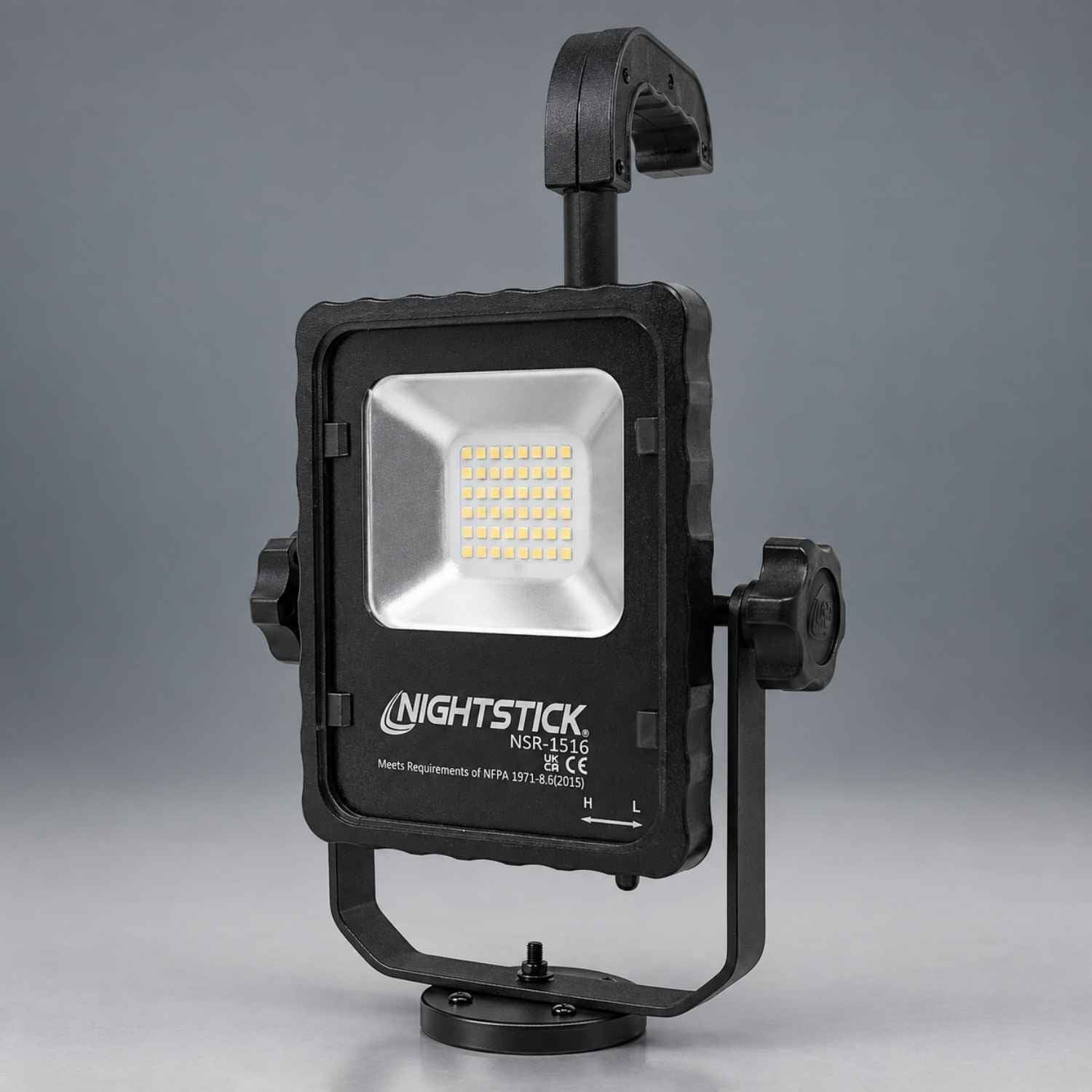 A black NIGHTSTICK LED floodlight with a mounting bracket and side adjustment knobs, shown on a neutral gray background.
