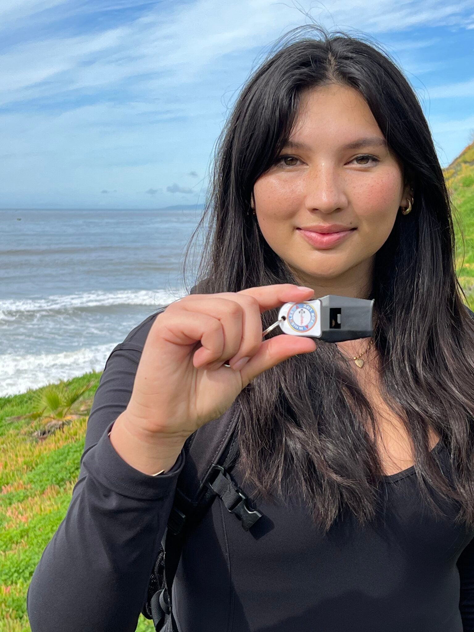 Woman holding a small whistle with a scenic background of water and sky.