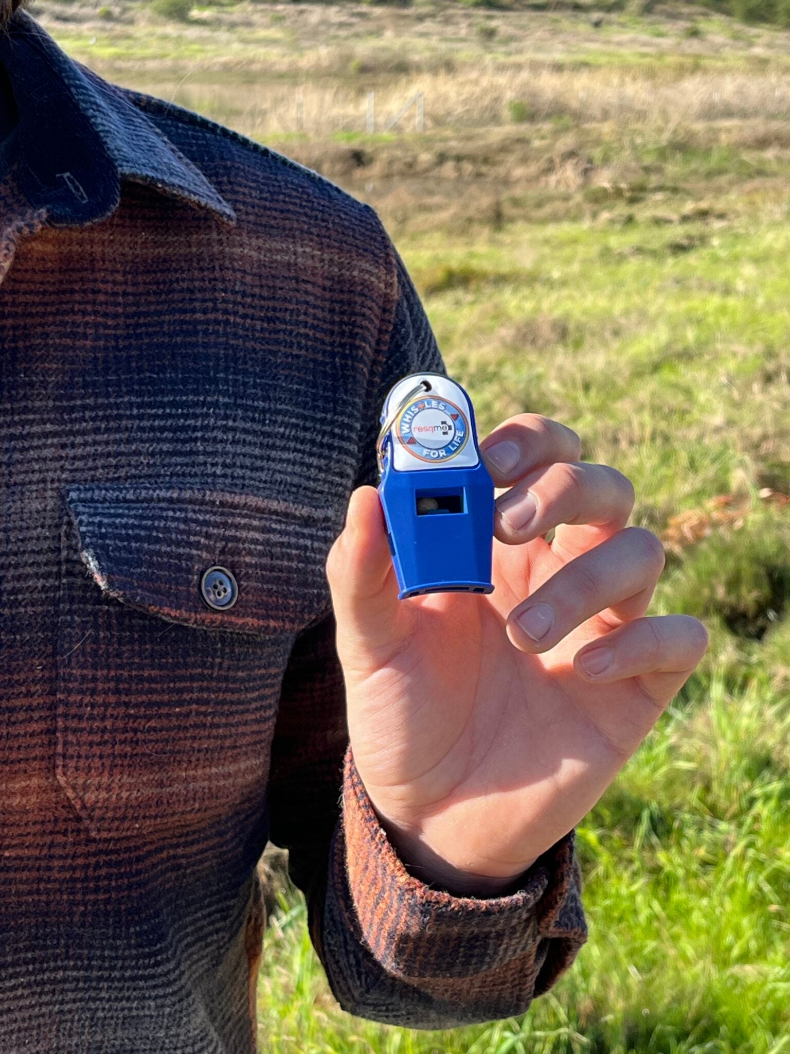 Person holding a blue whistle in a grassy field