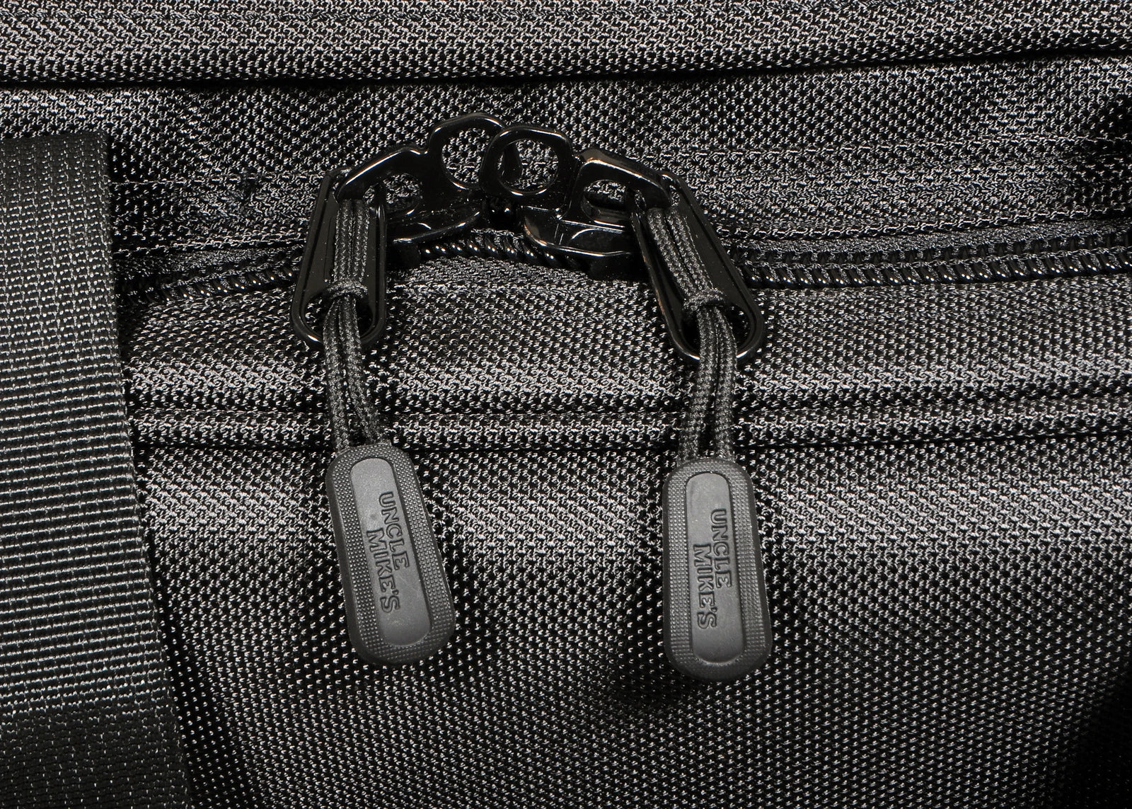 Close-up of a textured gray bag with black zippers and visible brand name.