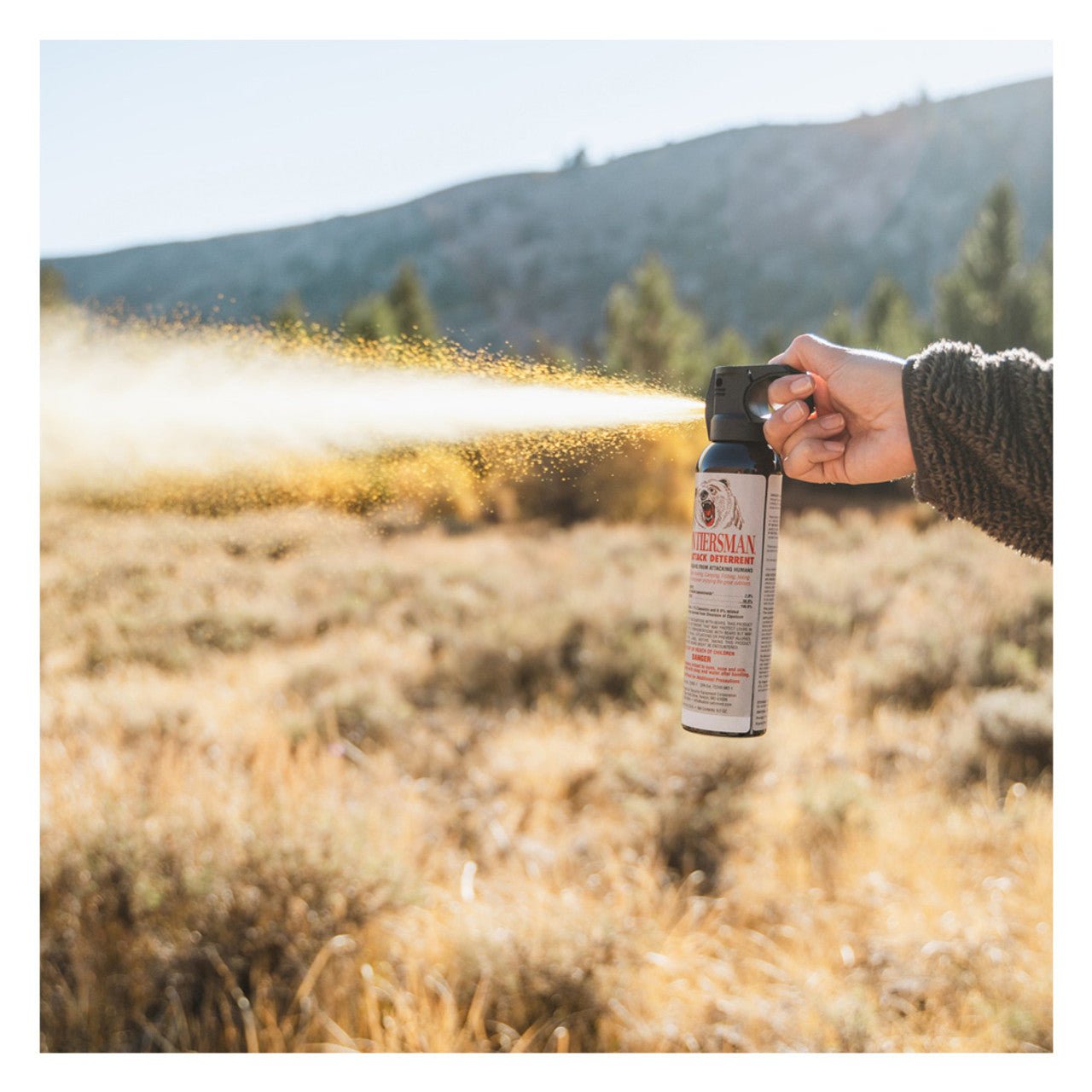 Person using a Sabre Frontiersman 9.2 oz Bear Attack Deterrent Spray in a field with mountains in the background
