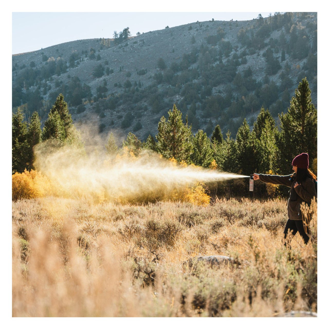 Person holding Sabre Frontiersman 9.2 oz Bear Attack Deterrent Spray in a field with mountains and trees in the background