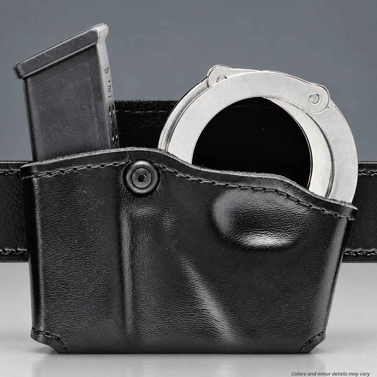 A black leather handcuff and magazine holster shown close-up against a gray background, containing a silver metal handcuff and a black magazine.