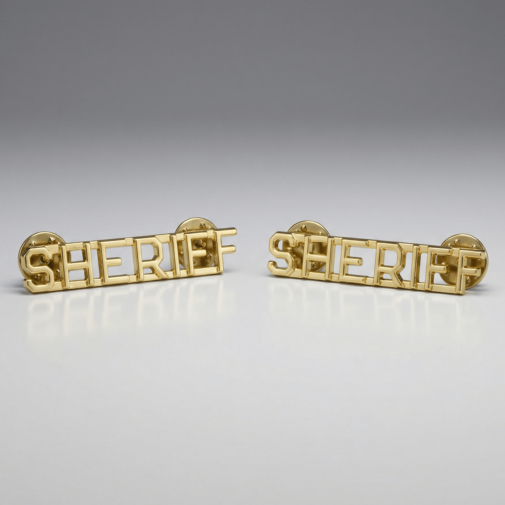 Two gold 'SHERIFF' pins on a gray background
