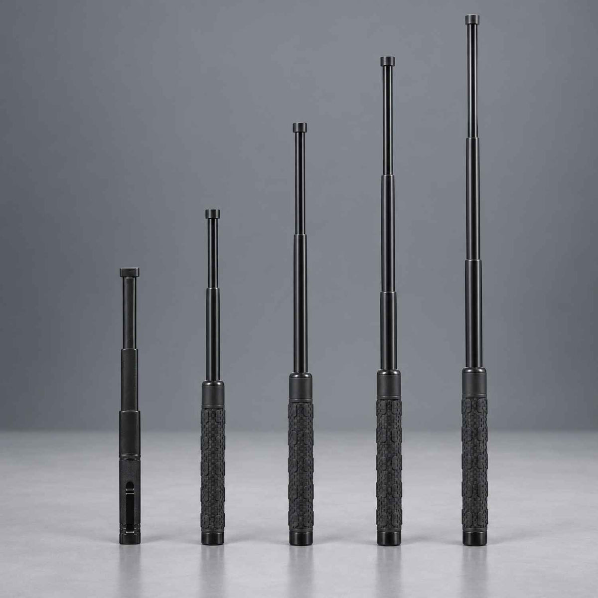 Five black telescoping batons or sticks with textured grips, arranged in ascending size order against a smooth gray studio background.