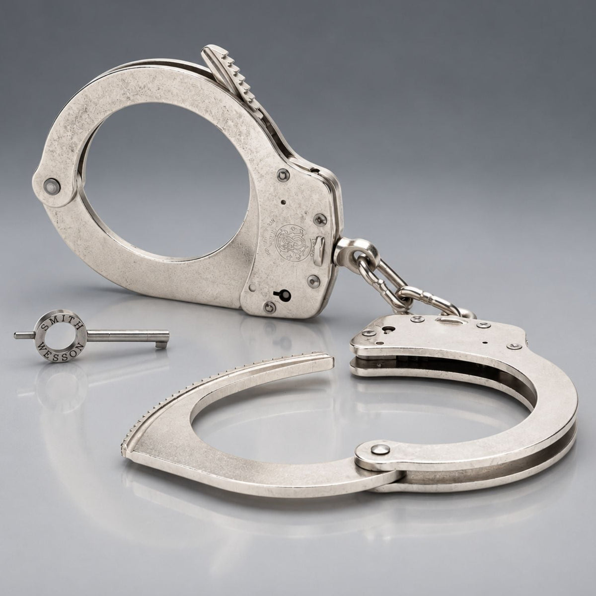 Smith & Wesson Model 1 nickel chain handcuffs 350132 shown open with one cuff unlocked, chain link, and S&W handcuff key
