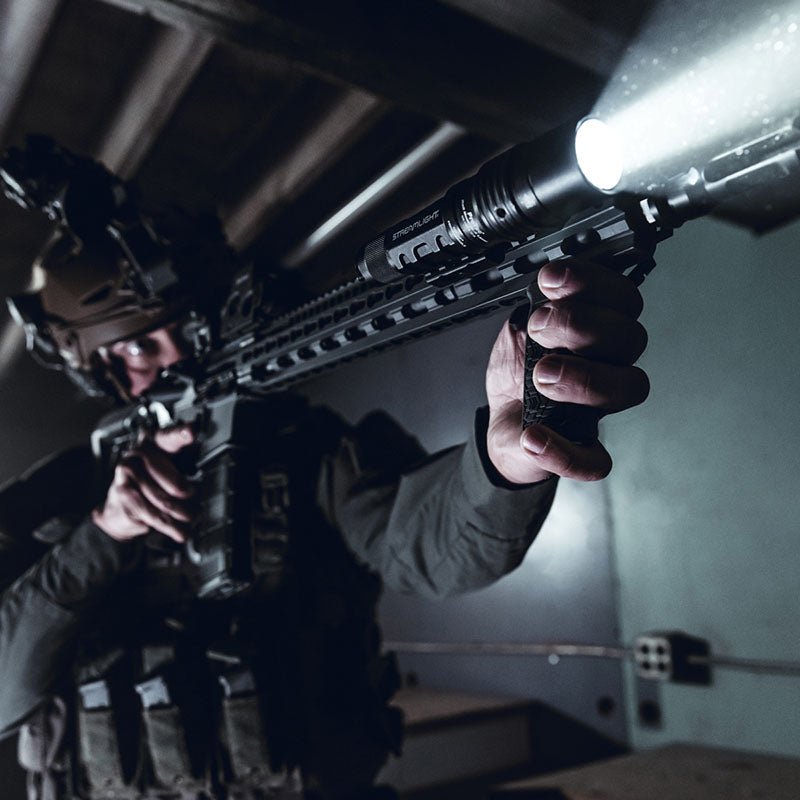Operator with a rifle-mounted Streamlight ProTac HL-X Laser lighting a dark building interior