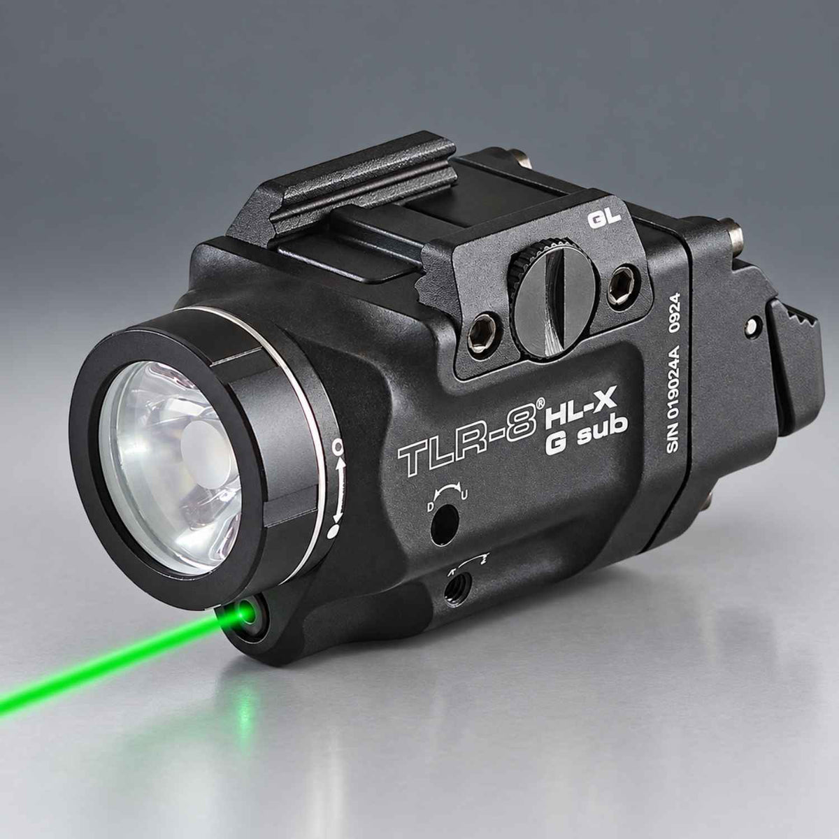 A black TLR-8 HL-X G sub laser sight with a green laser beam projecting from the front, shown on a reflective gray surface.