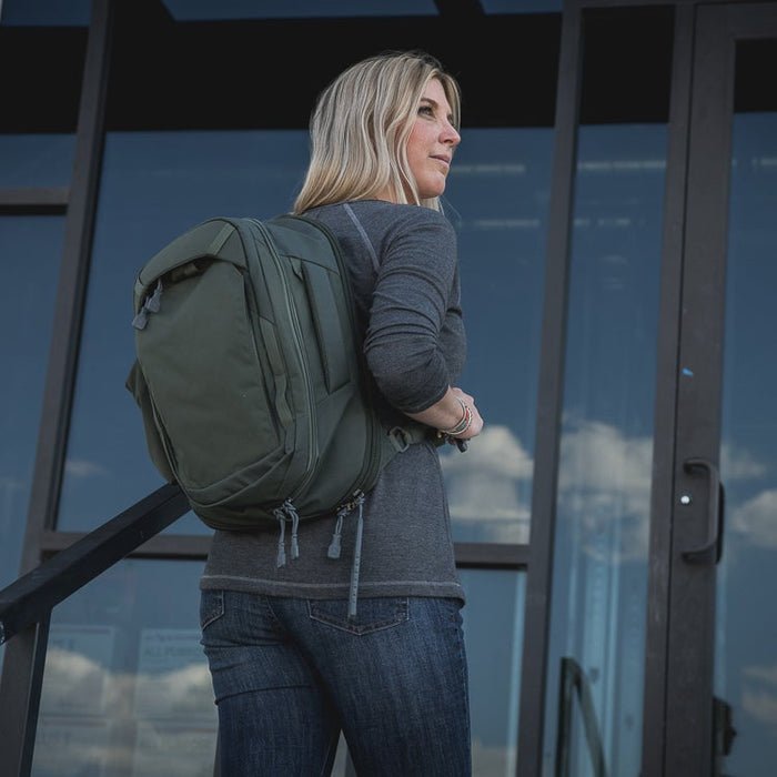 Person with a green backpack standing near a reflective surface