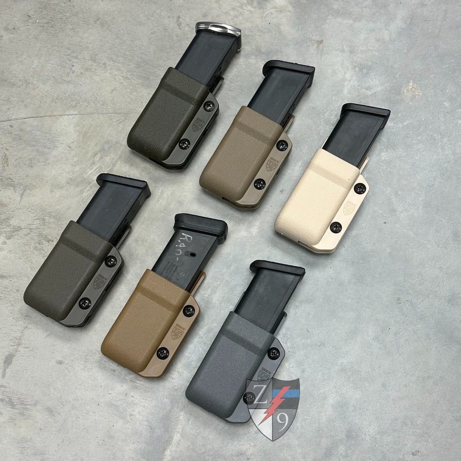 Set of six magazine holders in different colors on a gray surface with a brand logo in the corner.