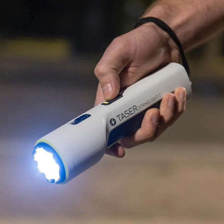 TASER StrikeLight 2 white stun gun flashlight illuminated, showing 700-lumen light beam